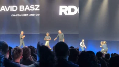 YouTuber invade palco de conferência da Roblox e protesta por mais segurança infantil na plataforma Criador conhecido como Emathiio interrompeu a abertura do Roblox Developers Conference 2026 enquanto o CEO David Baszucki entrava no palco. Vestindo uma camiseta com a frase “Kids deserve better”, ele foi rapidamente imobilizado pela segurança e retirado do evento. O episódio ocorre em meio à crescente pressão sobre a Roblox para ampliar mecanismos de proteção de crianças e adolescentes. Um protesto inesperado interrompeu por alguns segundos um dos momentos mais importantes do calendário anual da Roblox. Durante a abertura do Roblox Developers Conference 2026 (RDC), realizado em San Jose, na Califórnia, o YouTuber conhecido como Emathiio correu em direção ao palco no momento em que o cofundador e CEO da companhia, David Baszucki, iniciava sua participação. Enquanto avançava pelo palco, o criador gritou uma mensagem de protesto e revelou uma camiseta com a frase: “Kids deserve better” — “As crianças merecem algo melhor”. A intervenção durou poucos segundos. Um integrante da equipe de segurança o derrubou e, com auxílio de funcionários do evento, retirou o YouTuber do local. Baszucki não foi atingido e a apresentação prosseguiu normalmente. O protesto aconteceu diante do CEO da Roblox O momento escolhido não foi aleatório. A RDC é a principal conferência anual da Roblox voltada à comunidade de criadores e desenvolvedores. A edição de 2026 aconteceu entre 10 e 12 de setembro, no San Jose McEnery Convention Center, reunindo desenvolvedores, artistas e outros integrantes do ecossistema da plataforma. Na manhã de 11 de setembro estava programada justamente a principal apresentação do evento, com Baszucki e outros executivos discutindo novidades, produtos e os próximos passos da companhia. Foi durante essa abertura que ocorreu a invasão. Vídeos publicados nas redes sociais mostram Baszucki entrando no palco sob aplausos quando Emathiio aparece correndo atrás dele. O YouTuber grita: “We deserve better” — “Nós merecemos algo melhor”. Logo depois é interceptado. “Kids deserve better” A mensagem mais importante, entretanto, estava impressa na camiseta. KIDS DESERVE BETTER. O protesto fazia referência às críticas envolvendo a proteção de crianças dentro da Roblox, uma discussão que ganhou enorme repercussão nos últimos anos. Emathiio posteriormente confirmou que a intervenção tinha como objetivo chamar atenção para essa questão. Segundo ele, crianças afetadas por problemas dentro da plataforma normalmente não possuem espaço para falar em eventos corporativos como a RDC. O criador também argumentou que anos de progresso considerado lento na área de segurança representam mais tempo em que menores podem continuar expostos a riscos. Ele não pretendia interromper toda a conferência Emathiio afirmou posteriormente que seu objetivo não era encerrar a RDC nem prejudicar desenvolvedores e participantes. A intenção teria sido aproveitar a visibilidade do momento para levar a mensagem diretamente ao palco da empresa. Um dia antes do episódio, o YouTuber havia publicado um vídeo intitulado “roblox is completely unfixable”, no qual criticava diferentes decisões da companhia, incluindo sua relação com a comunidade e a forma como lida com segurança infantil. O protesto presencial acabou amplificando enormemente essa mensagem. Baszucki continuou a apresentação Depois que o manifestante foi retirado, David Baszucki retomou a abertura. O CEO reagiu ao episódio sem prolongar o confronto e fez uma breve referência bem-humorada à situação antes de continuar o evento. Não houve indicação de que ele tenha sofrido qualquer ferimento. Também não havia, nas informações públicas iniciais, confirmação de prisão do YouTuber. O que foi confirmado é que ele foi retirado da conferência. O episódio não surgiu em um vácuo O protesto acontece em um momento particularmente sensível para a Roblox. A empresa enfrenta questionamentos recorrentes sobre como protege sua enorme população de usuários menores de idade contra: assédio; aliciamento; conteúdo sexual inadequado; interações impróprias; comunicação entre adultos e menores. A própria Roblox estabelece em suas normas uma proibição explícita de exploração infantil, sexualização de menores, comportamento predatório, sextorsão e tentativas de aproximação de crianças para fins de exploração. A controvérsia não está, portanto, em saber se essas práticas são oficialmente permitidas. Elas não são. A discussão está em saber se as ferramentas, políticas e mecanismos de fiscalização empregados pela empresa são suficientes para detectá-las e impedi-las em uma plataforma gigantesca. O caso Schlep aumentou ainda mais a tensão Uma das controvérsias mais conhecidas envolve outro criador, chamado Schlep. Ele ganhou notoriedade produzindo vídeos nos quais tentava identificar supostos predadores que utilizariam a Roblox para entrar em contato com menores. A relação entre o criador e a companhia acabou se transformando em uma disputa pública. O episódio alimentou uma discussão muito maior sobre até onde criadores independentes deveriam ir para investigar possíveis predadores e quais responsabilidades cabem à própria plataforma e às autoridades. A controvérsia também se tornou parte do contexto citado em reportagens sobre o protesto de Emathiio. É importante separar denúncias de fatos comprovados A existência de denúncias e investigações relacionadas à segurança da Roblox não significa que toda acusação publicada contra usuários ou contra a própria plataforma esteja automaticamente comprovada. Também não é correto caracterizar a Roblox simplesmente como um ambiente em que a empresa “permite predadores”. A plataforma possui políticas contra exploração infantil e vem implementando controles adicionais. A crítica apresentada pelos manifestantes é diferente: eles consideram que as medidas adotadas ainda não são suficientes. Essa distinção é importante porque o debate envolve tanto casos reais de abuso quanto acusações que precisam ser analisadas individualmente. Roblox vem aumentando verificações de idade A companhia tem investido em sistemas destinados a separar melhor usuários por faixa etária e controlar determinadas formas de comunicação. Verificação de idade, controles parentais e restrições de interação fazem parte dessa estratégia. Essas medidas refletem um desafio especialmente complexo para uma plataforma cujo conteúdo é produzido pelos próprios usuários. A Roblox não funciona apenas como um catálogo de jogos tradicionais. Usuários podem criar experiências, conversar, formar comunidades, produzir itens e interagir em espaços virtuais. Quanto maior essa liberdade, maior também o desafio de moderação. O Brasil também entrou diretamente nessa discussão Para usuários brasileiros, a questão ganhou uma camada adicional em 2026. O ECA Digital, em vigor desde 17 de março, estabelece obrigações de proteção de crianças e adolescentes para serviços digitais acessíveis a esse público, incluindo jogos eletrônicos, redes sociais, aplicativos e plataformas de vídeo. A legislação envolve temas como proteção de dados, privacidade, supervisão parental, publicidade e mecanismos de verificação etária. A Roblox já criou orientações específicas para sua comunidade brasileira relacionadas à nova legislação e afirma ter ampliado controles destinados aos responsáveis de usuários menores de 18 anos no país. A proteção infantil virou uma questão regulatória global O debate não está acontecendo apenas dentro da comunidade gamer. Governos e autoridades de diferentes países passaram a pressionar plataformas digitais sobre a maneira como crianças utilizam seus serviços. A discussão envolve uma questão difícil: como permitir interação social e criatividade sem criar ambientes facilmente exploráveis por adultos mal-intencionados? Bloquear toda comunicação prejudicaria parte importante da experiência. Permitir comunicação irrestrita cria riscos evidentes. Sistemas de moderação automatizada ajudam, mas podem falhar. Moderação humana possui limitações de escala. Verificação de idade também apresenta desafios técnicos e de privacidade. Não existe uma solução única. A escala da Roblox torna tudo mais difícil O tamanho da plataforma amplia esse desafio. Roblox reúne uma enorme quantidade de experiências produzidas pela própria comunidade e uma população global de usuários. Isso significa que a companhia precisa moderar não apenas conteúdo criado internamente, mas um ecossistema em constante transformação. Um novo jogo pode aparecer. Um novo espaço social pode crescer rapidamente. Usuários podem encontrar novas maneiras de contornar filtros. Gírias mudam. Comportamentos abusivos se adaptam às ferramentas de moderação. É uma disputa permanente entre plataforma e abuso. Inteligência artificial virou parte da resposta da Roblox A empresa também aposta cada vez mais em IA para moderar conteúdo e desenvolver sistemas de segurança. Ao mesmo tempo, a própria expansão das ferramentas de inteligência artificial dentro da plataforma também gera questionamentos. Durante a RDC 2026, a Roblox apresentou diferentes iniciativas envolvendo criação assistida por IA, novas ferramentas para desenvolvedores e formas de ampliar a distribuição das experiências produzidas na plataforma. Isso significa que a empresa está tentando expandir justamente no momento em que enfrenta pressão para demonstrar que consegue controlar os riscos do ecossistema atual. É uma tensão importante para o futuro da companhia De um lado, a Roblox quer: mais usuários; mais criadores; mais experiências; mais inteligência artificial; mais plataformas; mais formas de distribuição. Do outro: quanto maior o ecossistema, maior a superfície de moderação. Esse equilíbrio entre crescimento e segurança pode se tornar uma das questões centrais para a empresa nos próximos anos. Emathiio transformou uma camiseta em uma mensagem global O protesto durou segundos. Mas foi construído para funcionar perfeitamente na lógica das redes sociais. Um grande evento. O CEO entrando no palco. Uma pessoa correndo. Segurança intervindo. E uma frase enorme estampada em uma camiseta: KIDS DESERVE BETTER. O vídeo rapidamente ganhou circulação fora da própria conferência. E isso demonstra uma característica dos protestos contemporâneos. O público presente fisicamente pode ser relativamente pequeno. O público real está na internet. A invasão do palco também levanta uma questão de segurança física Independentemente da motivação do protesto, conseguir correr até o palco durante a entrada do CEO representa uma falha relevante de controle físico do evento. A segurança reagiu rapidamente. Mas o manifestante conseguiu chegar suficientemente perto do palco para interromper a abertura. Em eventos corporativos envolvendo executivos conhecidos, esse tipo de situação costuma provocar revisão de: credenciamento; controle de acesso; posicionamento de seguranças; barreiras físicas; procedimentos de entrada no palco. Não há indicação pública de que Emathiio pretendesse atacar fisicamente Baszucki. Seu comportamento foi apresentado como protesto. Ainda assim, a equipe de segurança não tinha como saber isso no instante em que uma pessoa corria em direção ao palco. Protesto chama atenção, mas não resolve o problema O episódio provavelmente será lembrado como um dos momentos mais inesperados da RDC 2026. Mas a discussão levantada por ele é muito maior. A Roblox precisa equilibrar crescimento, liberdade criativa, comunicação social e proteção de uma enorme comunidade de menores. Criadores críticos argumentam que a evolução das medidas de segurança é lenta demais. A empresa, por outro lado, vem ampliando mecanismos de verificação, controles parentais e restrições de comunicação, além de afirmar que segurança é uma prioridade central da plataforma. O desafio será medir se essas ferramentas produzem resultados suficientes na prática. Porque, para uma plataforma com forte presença entre crianças e adolescentes, segurança não pode ser apenas uma configuração dentro do aplicativo. Ela se tornou uma questão de confiança. E foi exatamente essa discussão que Emathiio conseguiu colocar no centro da principal conferência anual da Roblox ao correr para o palco com apenas quatro palavras estampadas na camiseta: “Kids deserve better.” Slug: youtuber-invade-palco-roblox-rdc-2026-protesto-seguranca-infantil Meta description: YouTuber Emathiio invadiu o palco da Roblox Developers Conference 2026 durante a entrada do CEO David Baszucki para protestar por mais segurança infantil na plataforma. Categoria: Games & Jogos